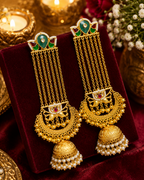 A pair of ornate gold-toned Indian jhumka earrings with green and red enamel details.